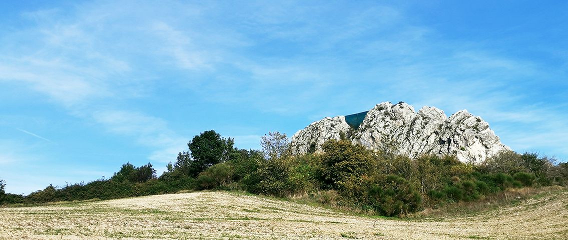 Un affioramento roccioso chiaro emerge da un prato sotto il cielo azzurro